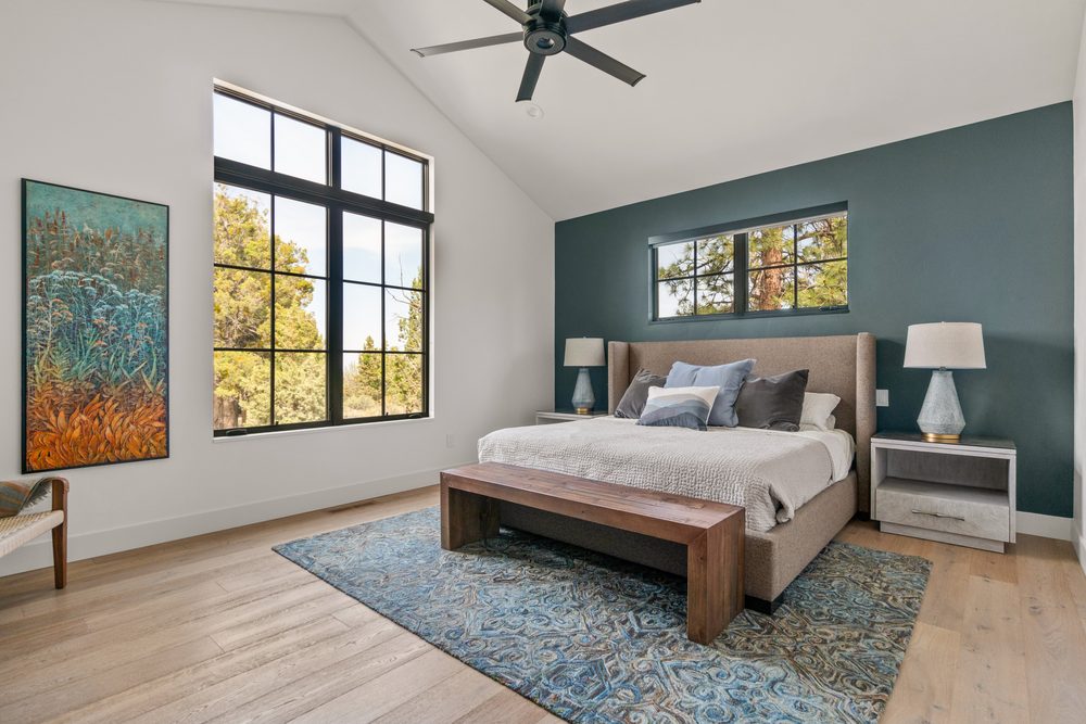 Primary bedroom with vaulted ceiling, accent wall, and forest views